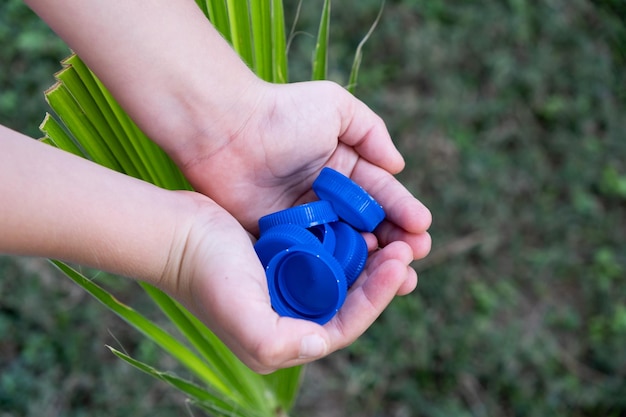 Blue plastic bottle caps in baby palms collecting plastic\
bottle caps for further processing