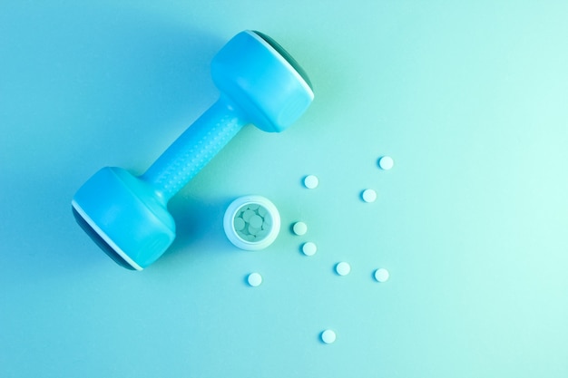 Фото Синяя пластиковая гантель и бутылка с белыми витаминными таблетками
