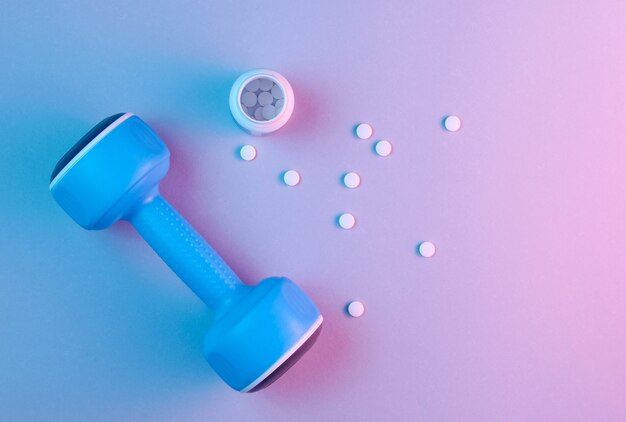 Blue plastic dumbbell and bottle with white vitamin pills