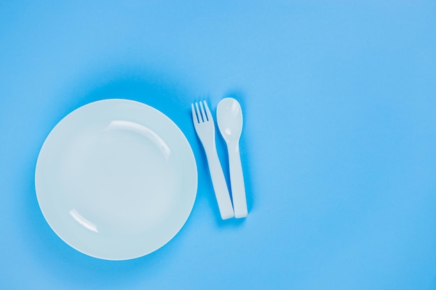 Blue plastic plate with spoon and fork on blue background