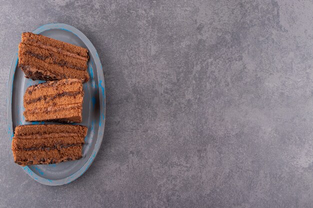 Blue plate of chocolate cake placed on stone table.