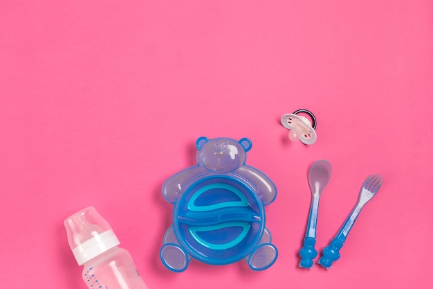 Blue plate in the form of a bear a bottle knife and spoon on pink table children dinner time top view