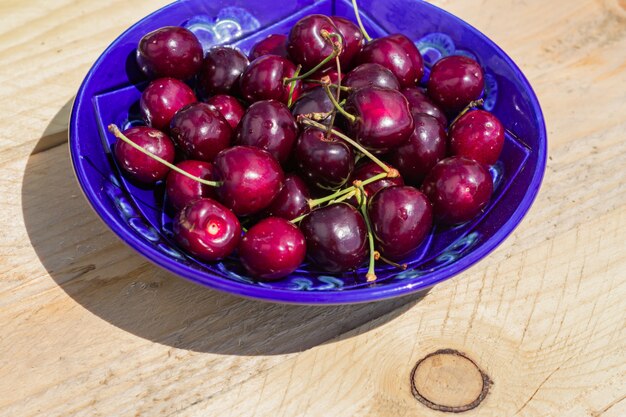 Blue plate of ripe sweet cherry on  wooden table