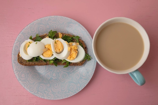 On a blue plate there is grain bread with greens and an egg and a cup of coffee top view the concept of a proper nutrition breakfast