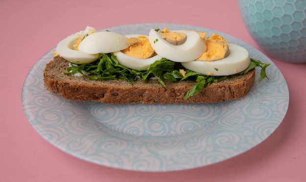 Photo on blue plate there is grain bread with greens and an egg on pink background the concept of breakfast healthy food