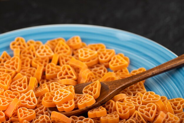 Blue plate of uncooked dry pasta on black background. 