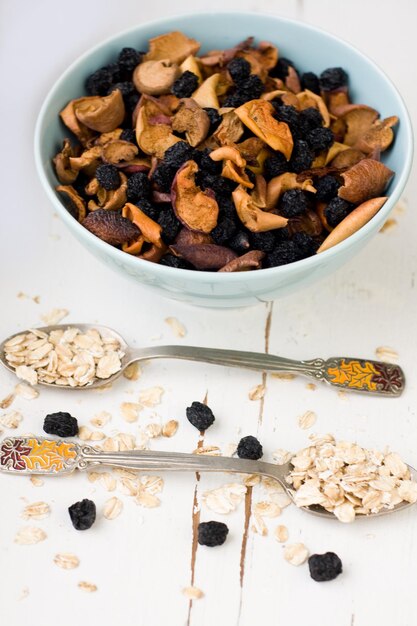 Foto piatto blu con mele secche e frutti di bosco e un cucchiaio di farina d'avena su uno sfondo di legno bianco cibo sano