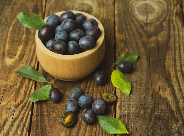 Blue plum in a bowl on a wooden table Fruit background with copy space