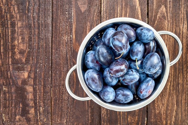 Blue plums in rustic colander on old wooden table.