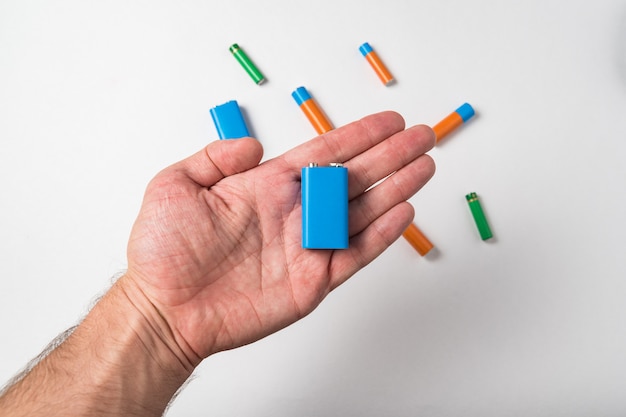 Blue PP3 battery in male hand on white background. Different types of accumulatores.