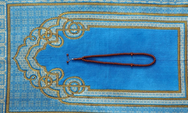 A blue prayer rug in the house of a Muslim his rosary next to it a prayer rug for worship in Islam