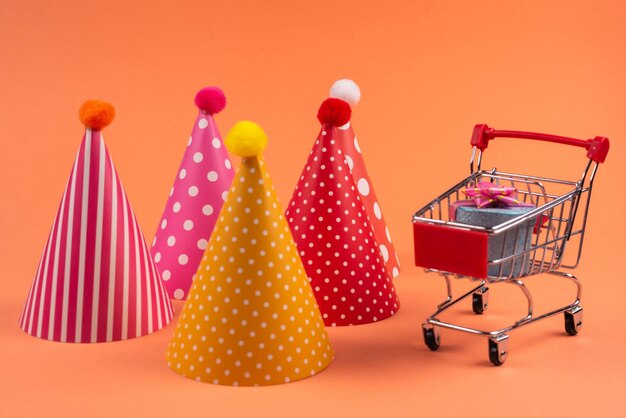 Blue present box with pink bow in a shopping cart and birthday cap on a red background