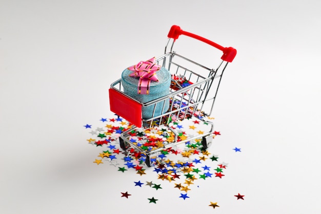 Blue present box with pink bow in a shopping cart and confetti