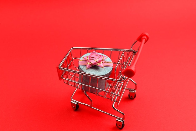 Blue present box with pink bow in a shopping cart on a red background