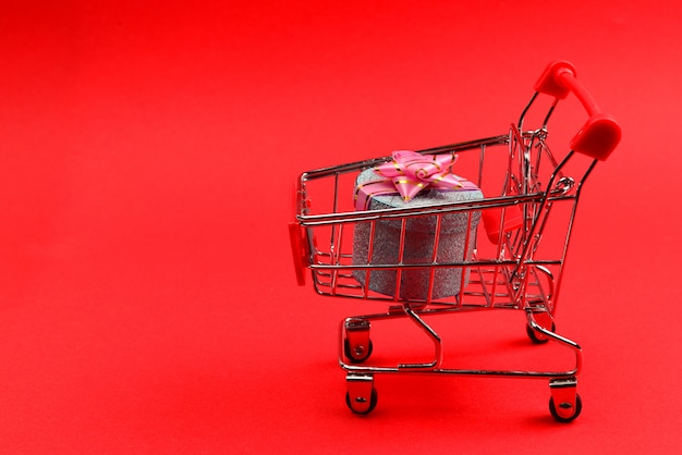 Blue present box with pink bow in a shopping cart on a red background.