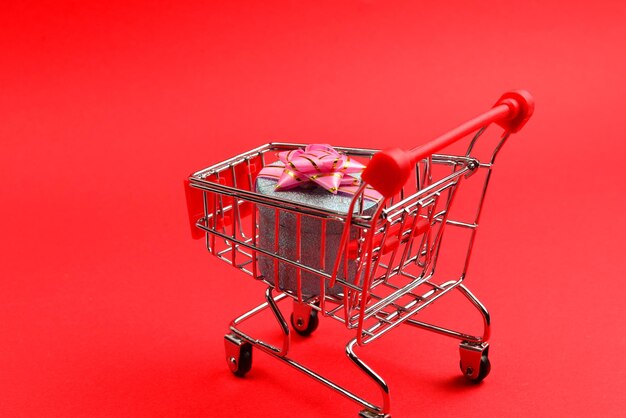 Blue present box with pink bow in a shopping cart on a red background