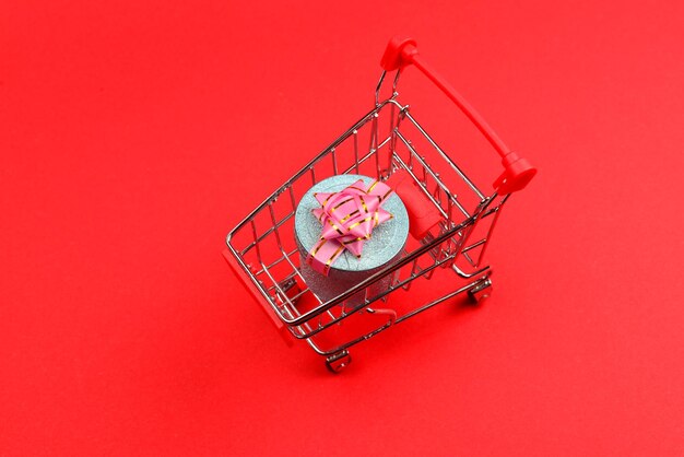 Blue present box with pink bow in a shopping cart on a red background