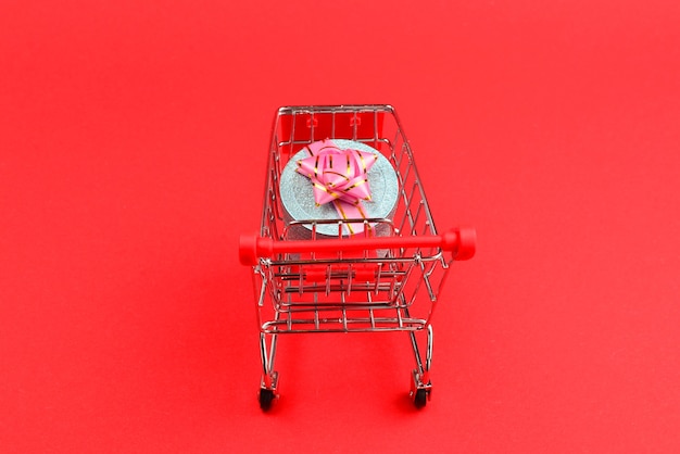 赤い背景のショッピングカートにピンクの弓と青いプレゼントボックス。
