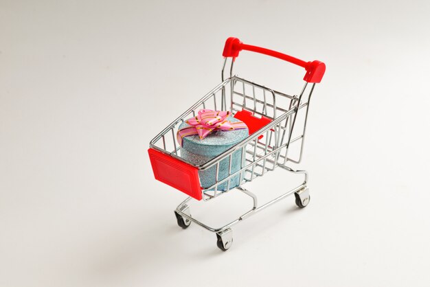 Blue present box with pink bow in a shopping cart on a white background.