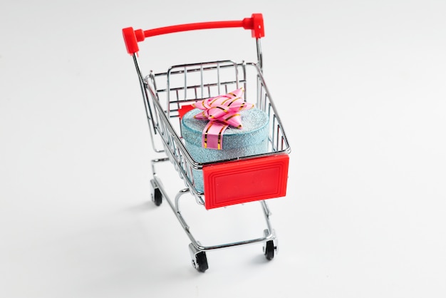 Blue present box with pink bow in a shopping cart on a white