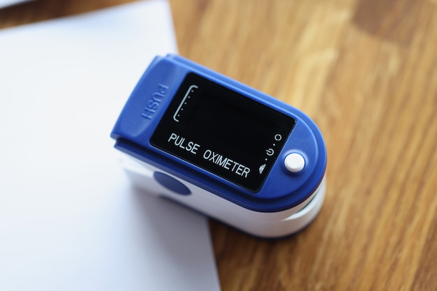 Photo blue pulse oximeter lying on wooden table with documents closeup diagnostics covid concept