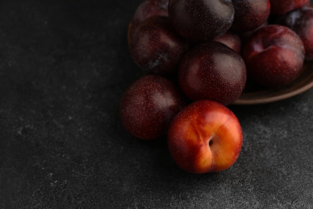 Blue and red pears in ceramic plate on dark stone textured table. Red plum in the foreground. Selective focus.