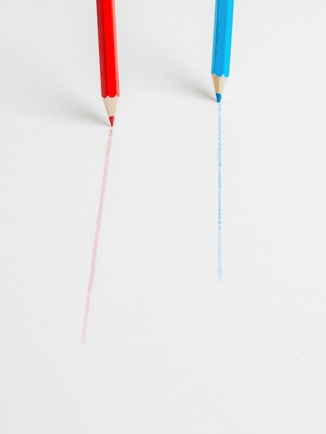 Blue and red pencils drawing parallel lines on a white surface. The concept of cooperation.