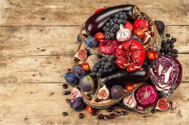 Blue, red and purple food. Culinary background of fruits and vegetables. Fresh figs, plums, onion, eggplant, grape, cabbage, apple, garlic, dogwood, pomegranate, beetroot. Wooden stands and old boards