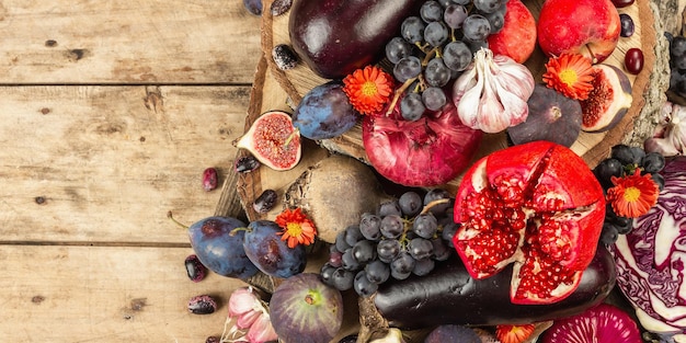 Blue, red and purple food. Culinary background of fruits and vegetables. Fresh figs, plums, onion, eggplant, grape, cabbage, apple, garlic, dogwood, pomegranate, beetroot. Wooden stands and old boards