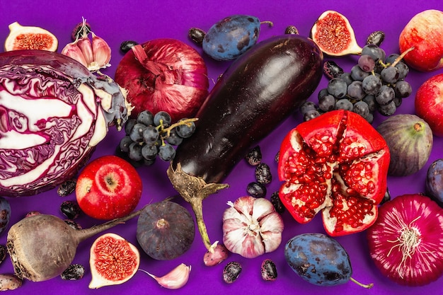 Cibo blu, rosso e viola. sfondo culinario di frutta e verdura. fichi freschi, prugne, cipolla, melanzane, uva, cavoli, mele, aglio, cornioli, melograni, barbabietole. sfondo viola, disposizione piatta