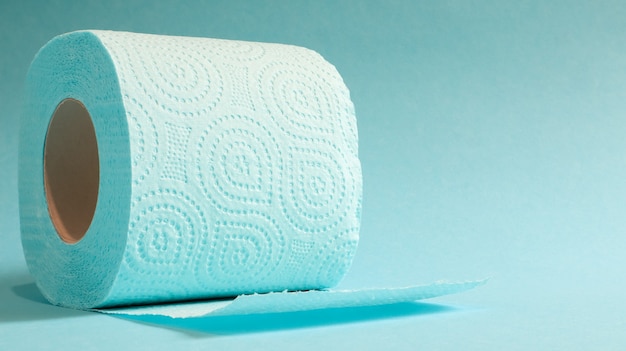 Blue roll of modern toilet paper on a blue background. a paper\
product on a cardboard sleeve, used for sanitary purposes from\
cellulose with cutouts for easy tearing. embossed drawing. copy\
space.