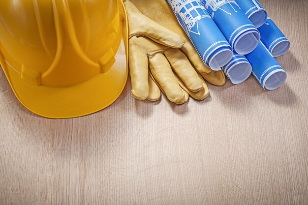 Photo blue rolled construction drawings building helmet leather protective gloves on wooden board