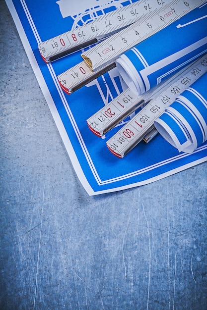 Blue rolled construction plans wooden meter on scratched metallic background