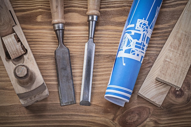 Blue rolled up construction drawing planer chisels wooden studs on wood board.