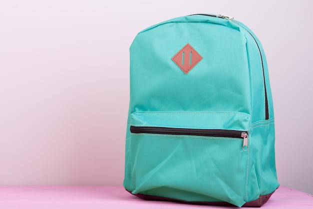 Blue school backpack is on a pink wooden table on pink background