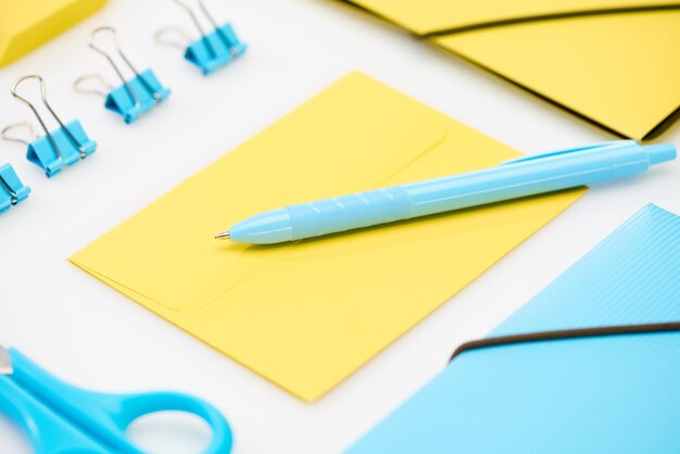 Blue scissors paper clips folder and pen on yellow envelope near yellow folder on white background