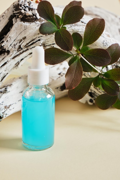 Blue serum in a transparent dropper bottle on the background of a wooden snag and branches