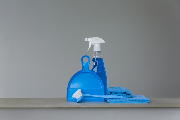 Foto insieme blu degli strumenti e del prodotto di pulizia su superficie neutra.