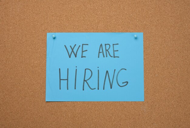 Photo blue sheet of paper with an inscription we are hiring on a brown cork board. recruitment