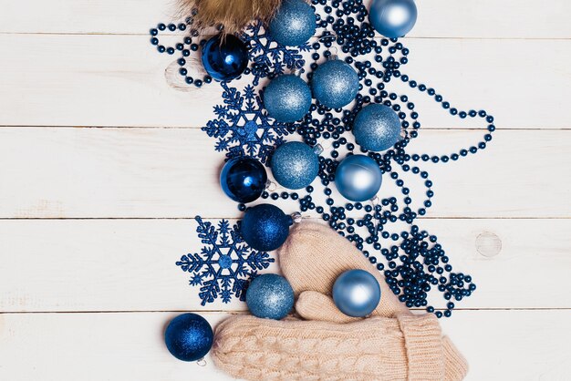 Blue shiny Christmas decorations, balls, stars and beads, coffee on a wooden table with a knitted hat and beige mittens, flat lay, top view. Winter cozy, new year, holiday concept.