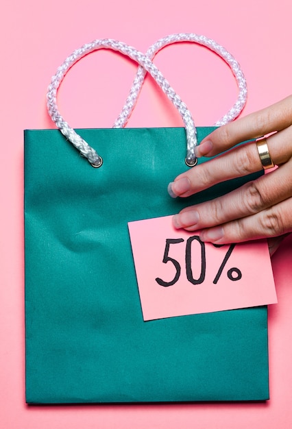 blue shopping bag with a sticker that says 50% discount and woman hand on a bright pink surface