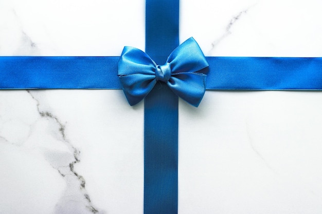 Blue silk ribbon and bow on luxury marble background holiday flatlay backdrop