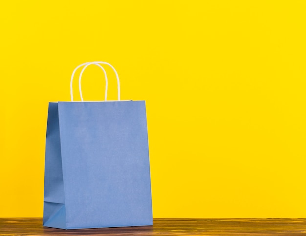 Blue single paper bag on wooden surface with yellow backdrop