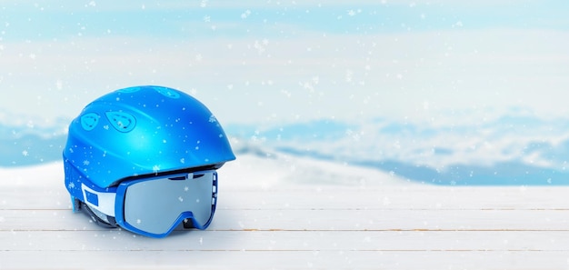 Синий лыжный шлем и очки на белом деревянном столе Место для свободного текста рядом со снежными вершинами гор на заднем плане