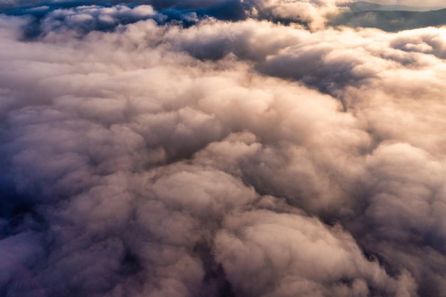 탁 트인 전망 아래 산봉우리가 있는 밝은 주황색 일출의 두꺼운 흰색 솜털 구름 위의 푸른 하늘