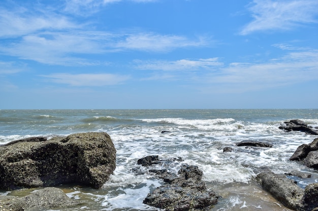 Under the blue sky, the waves beat the rocks on the beach