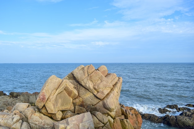 Under the blue sky, the waves beat the rocks on the beach