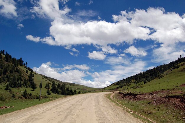 Under the blue sky and white clouds there is an empty dirt road leading to the distance