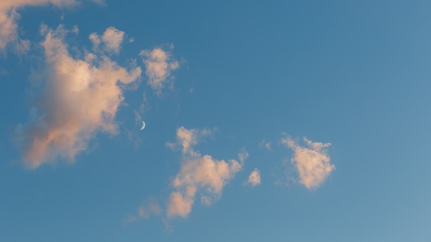 Cielo azzurro con nuvole rosa al tramonto e il mese.