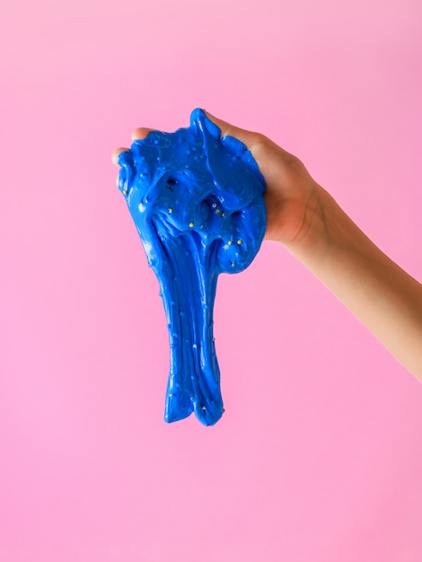 Blue slime falls from the hands of a child on a pink.